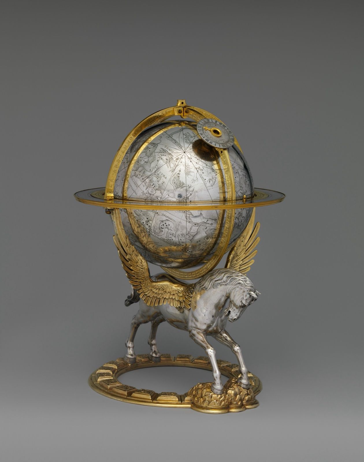 A silver celestial globe engraved with constellations, set in gilded rings and carried by a winged horse, on a grey ground.