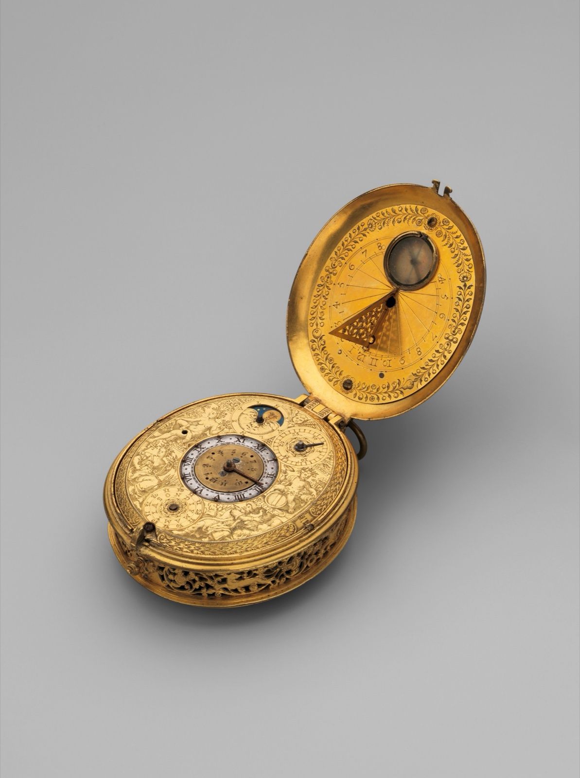 A gilded watch with its lid open: an astronomical dial below, a small sundial and compass inside the lid, on a grey ground.