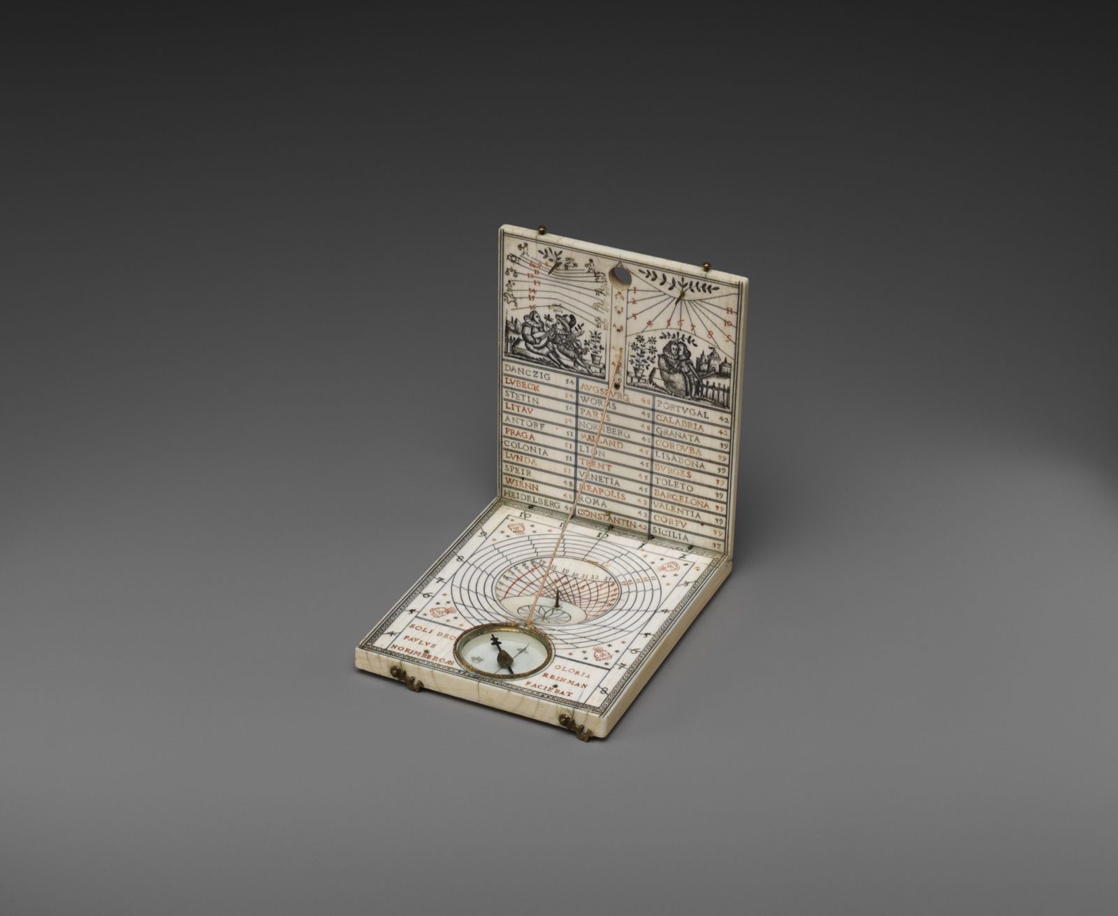 A small ivory folding sundial standing open, its upright leaf engraved with tables, a compass in its base, on a dark grey ground.